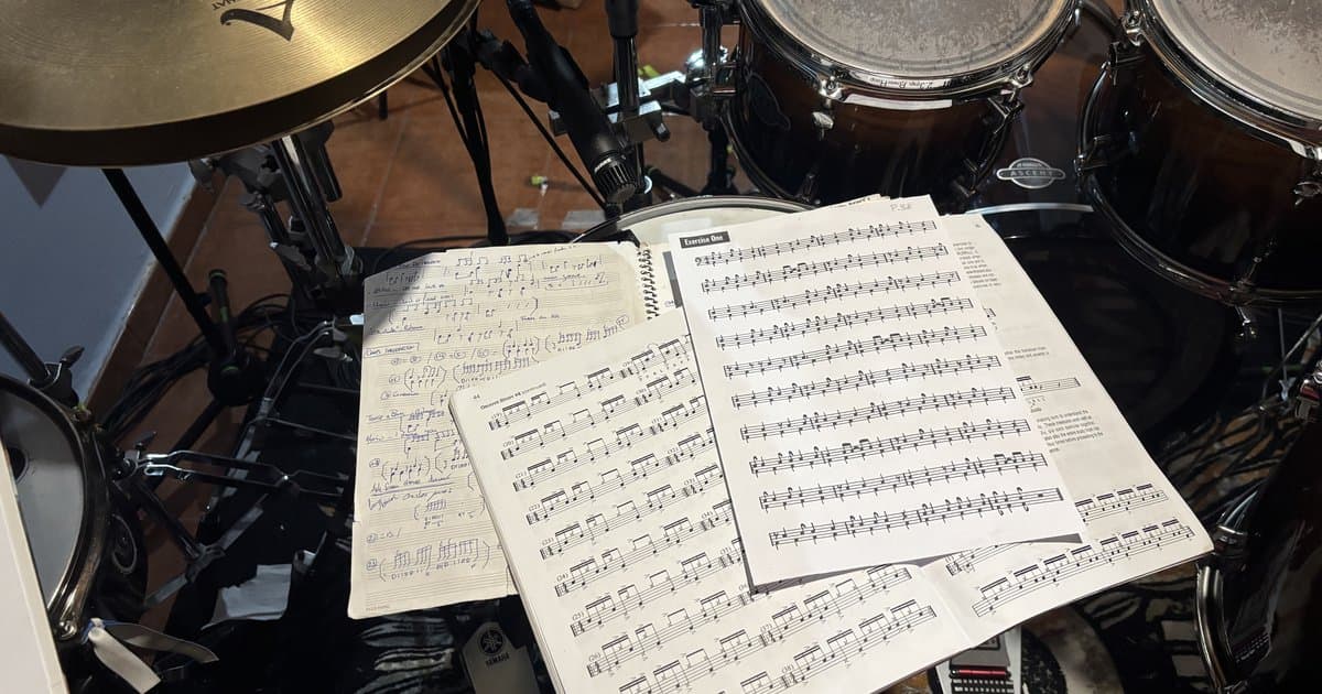 Dos cuadernos de partituras de batería abiertos sobre el set, con platos y toms alrededor